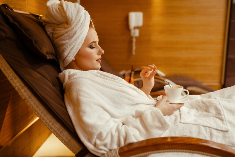 Sexy girl in bathrobe and towel on the head relaxing with cup of coffee in spa chair. Relaxation leisure, healthy lifestyle, attractive woman resting in armchair, beauty salon