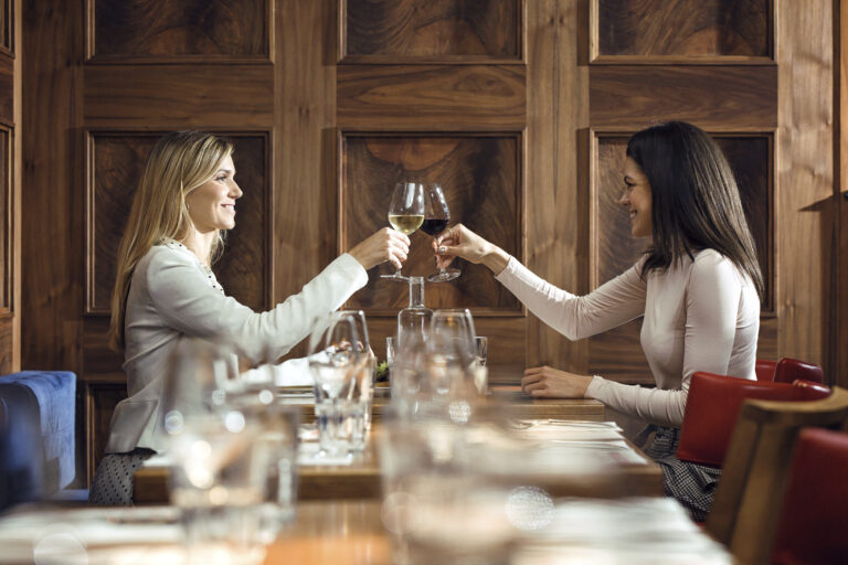 Two businesswomen clinking wine glasses in a restaurant